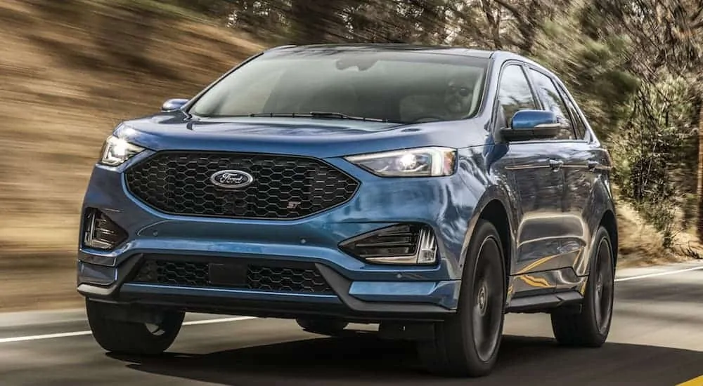 A blue 2020 Ford Edge is driving on a treelined road. 