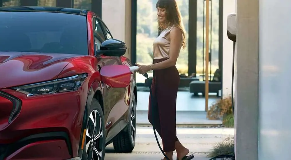 A woman is charging her red 2021 Ford Mustang Mach-E at home. 