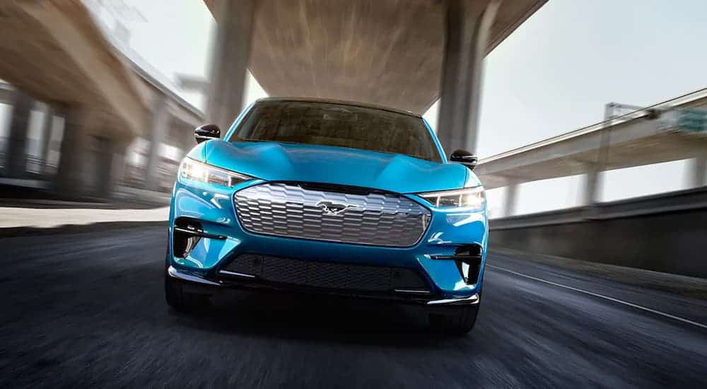 A blue 2021 Ford Mustang Mach-E GT is driving under a bridge while facing forward.