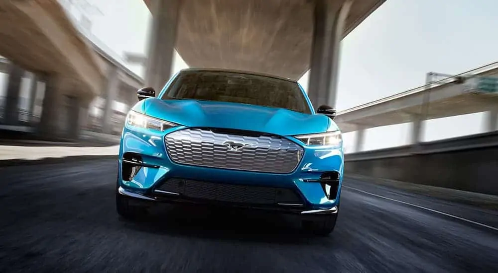 A blue 2021 Ford Mustang Mach-E GT is driving under a bridge while facing forward.