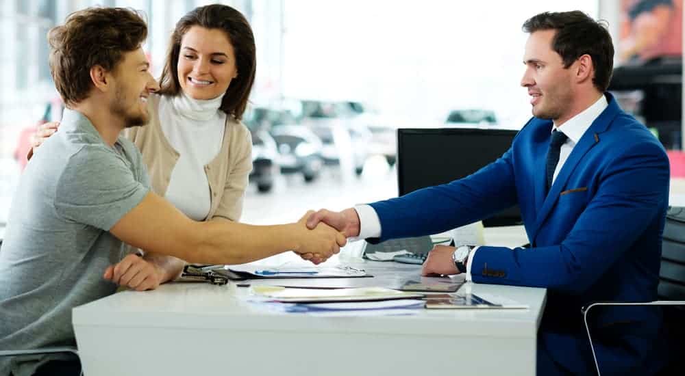 A smiling customer is shaking the hand of a car salesman.