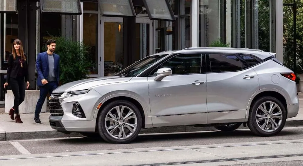 A smiling couple is walking to their silver 2020 Chevy Blazer, which is a popular option among Chevy SUVs, that's parked in front of a restaurant. 