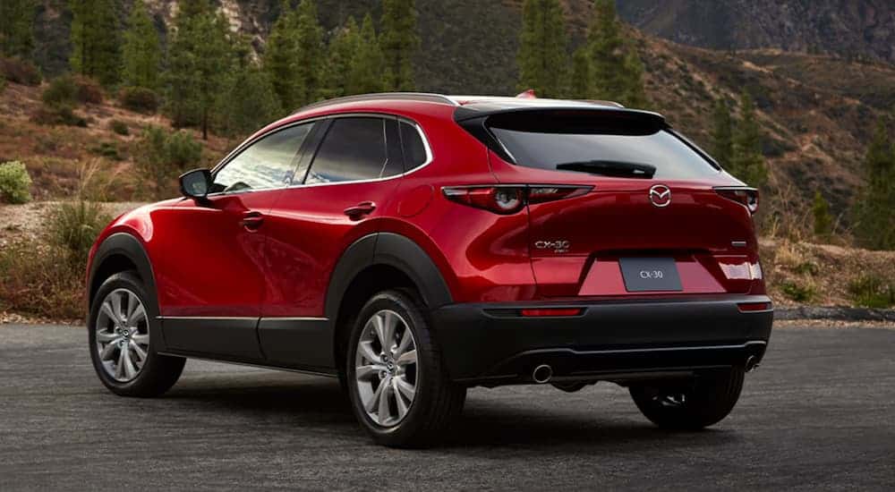 A red 2020 Mazda CX-30 is parked next to a wooded trail in the mountains. 