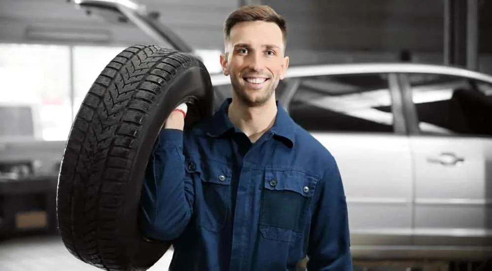 A smiling mechanic is holding a tire at a local tire shop near me. 