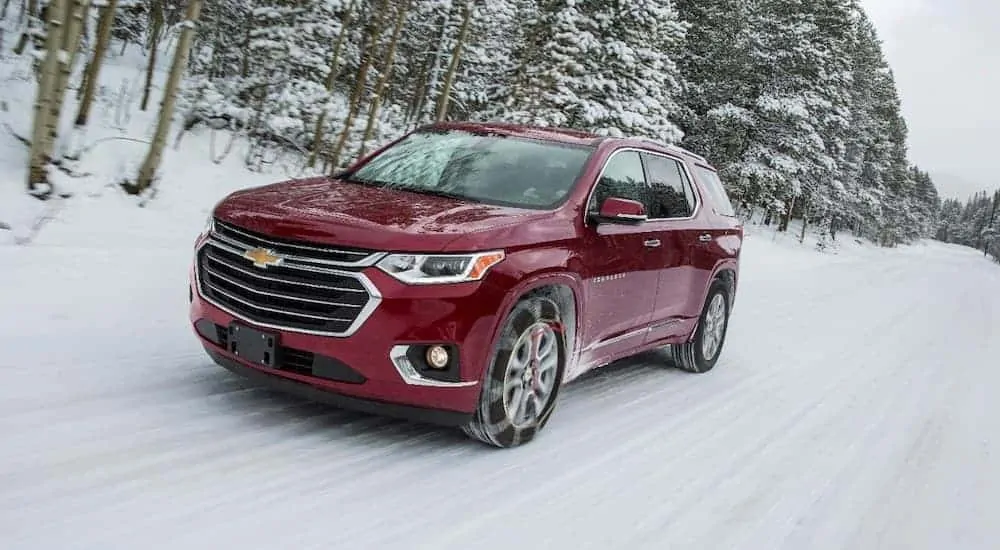 A red 2018 Chevy Traverse is driving in the snow after leaving a used car dealership near me.