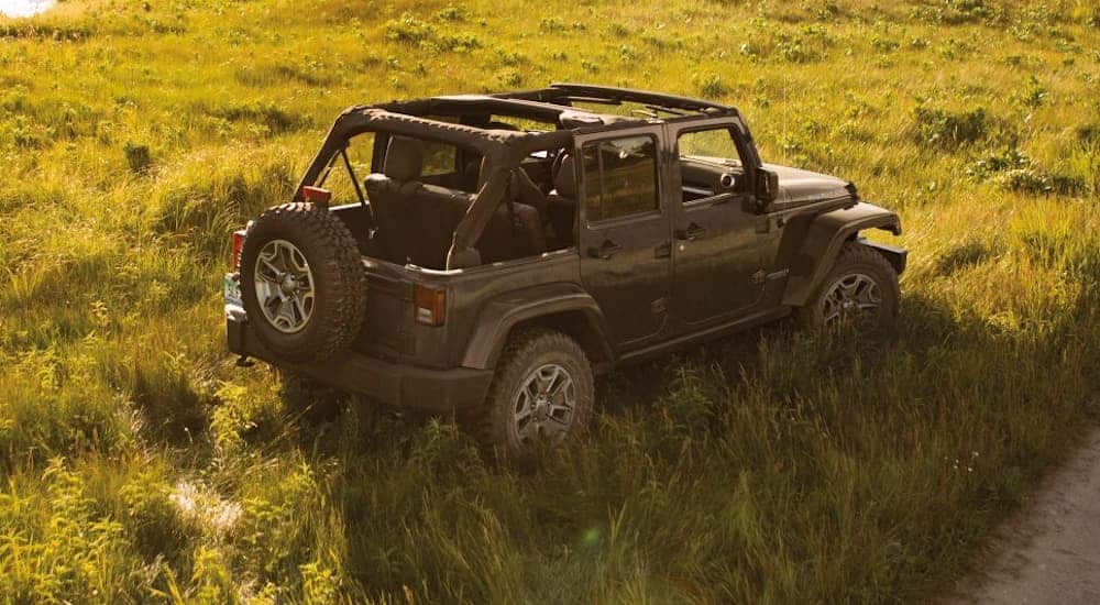 A birds eye view of a grey 4-door 2016 Jeep Wrangler is parked in a grassy field off of a dirt trail.