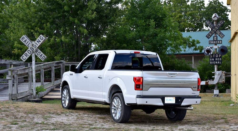 A white 2018 Ford F-150 SuperCrew Cab is parked on grass next to a railroad crossing.