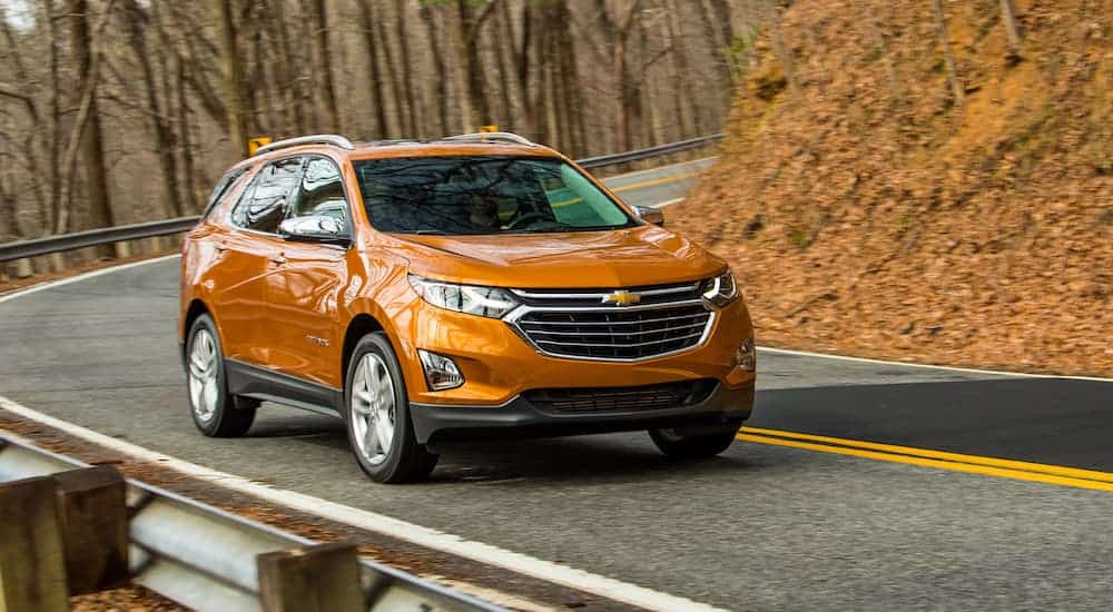 An orange 2019 Chevy Equinox is driving around a corner on a curvy tree lined road during the fall season.