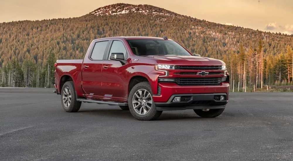A red 2020 Chevy Silverado 1500 with a diesel engine, which wins when comparing the 2020 Chevy Silverado vs 2020 Ram 1500, is parked in a parking lot with mountains in the distance. 