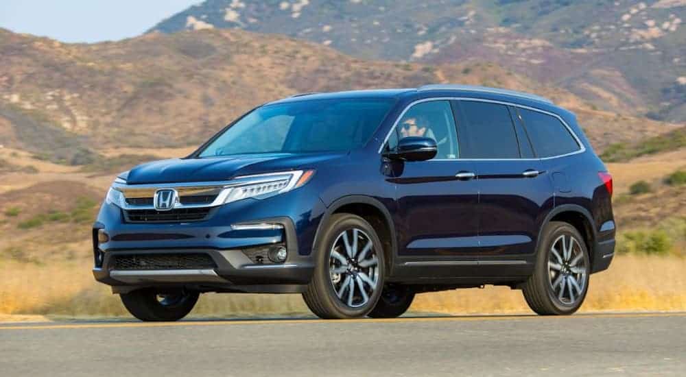 A blue 2020 Honda Pilot is driving on a highway with mountains in the distance. 