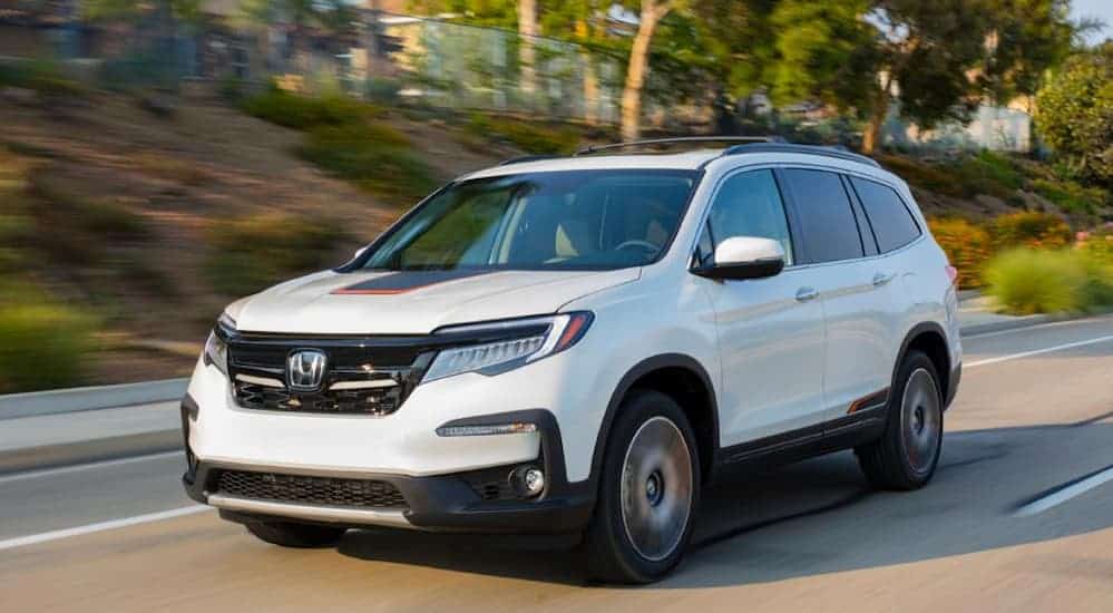 A white 2020 Honda Pilot is driving on a treelined road.