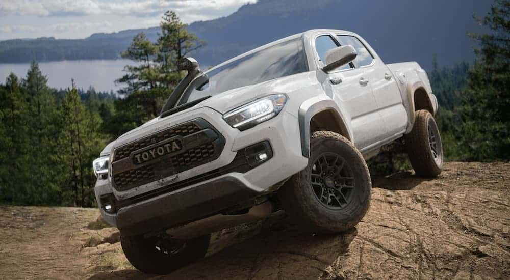 A white 2020 Toyota Tacoma is parked on a rock in front of a mountain and lake.