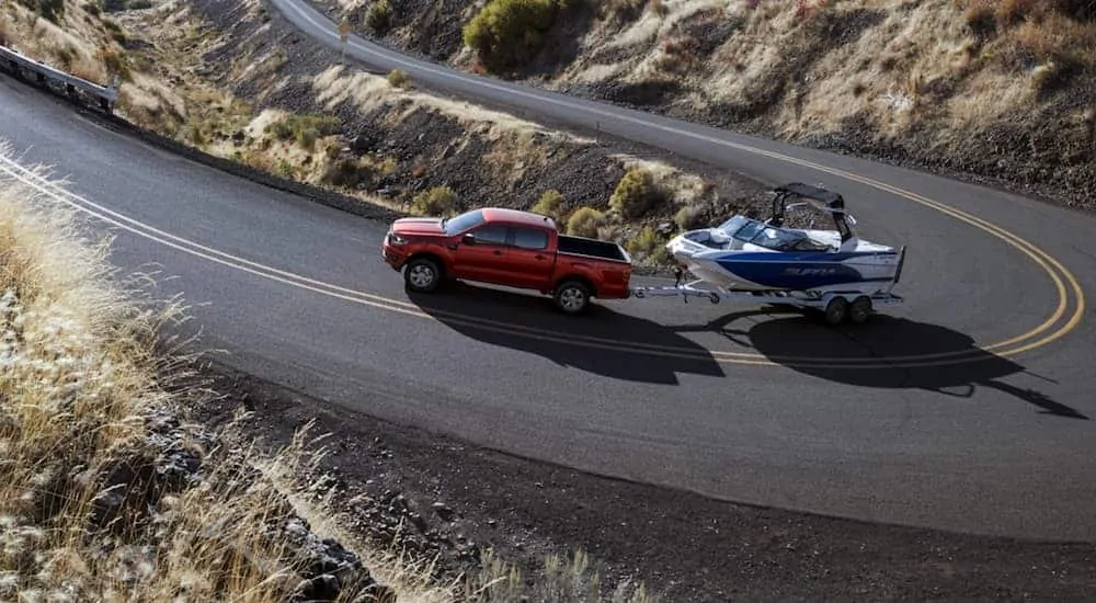 A red 2020 Ford Ranger is towing a boat on a winding road.