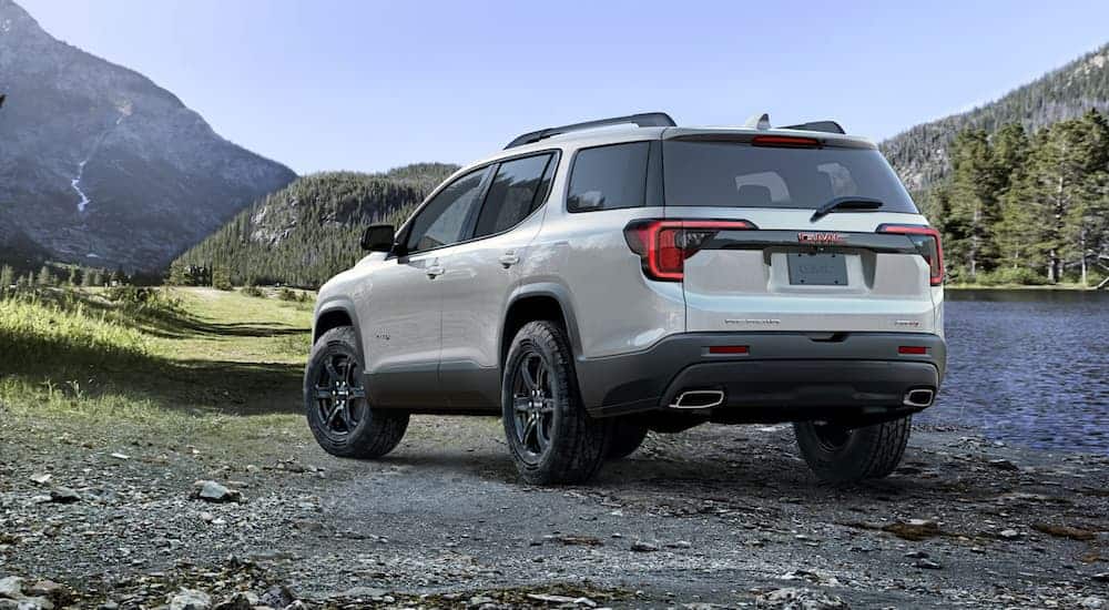 A white 2020 GMC Acadia AT4 is parked next to a lake and mountains.