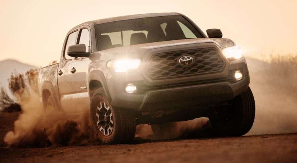 A grey 2020 Toyota Tacoma is driving through dirt at dusk.