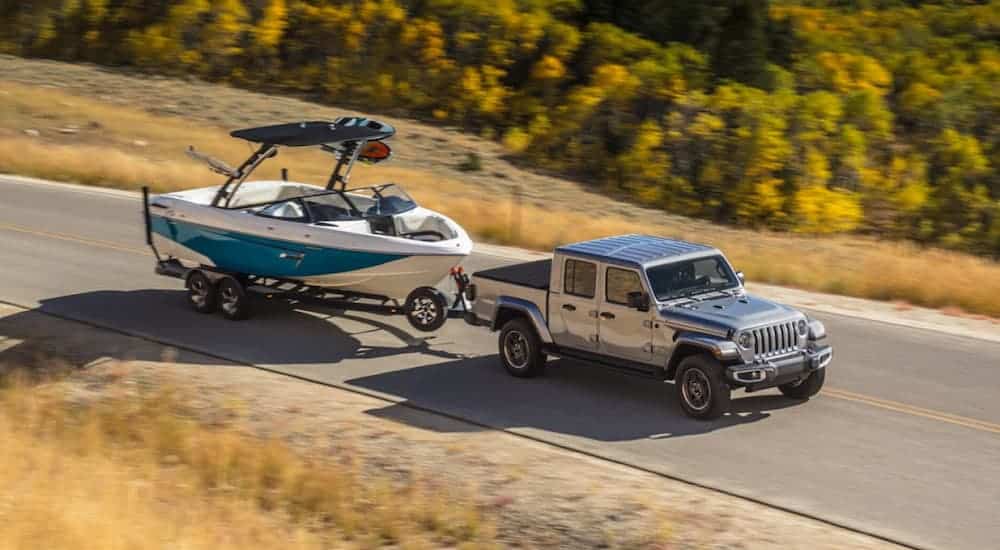 A grey 2020 Jeep Gladiator is towing a large boat up a tree lined hill. 