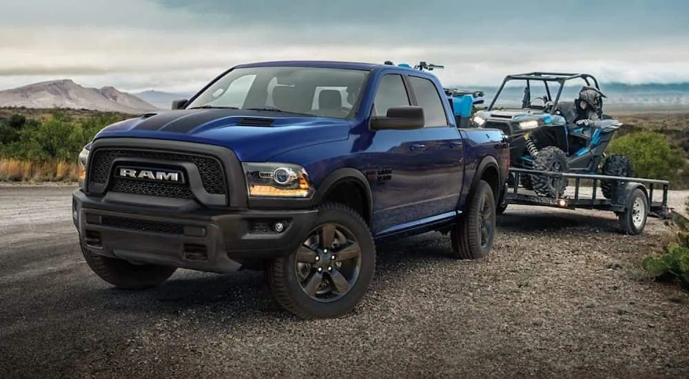 A blue 2019 Ram 1500 Classic in the Warlock edition is towing a side-by-side.