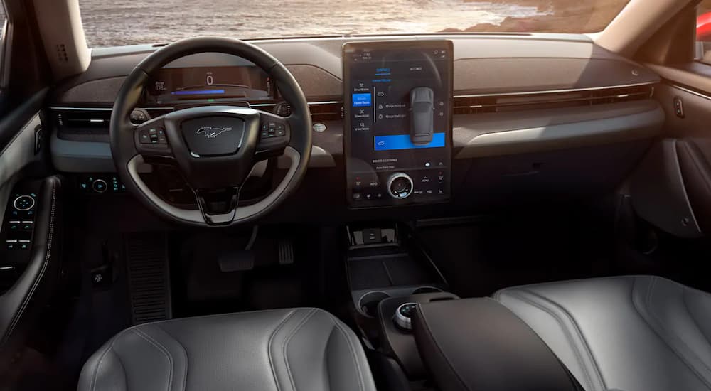 The front grey leather interior of a 2021 Ford Mustang Mach-E is shown with an infotainment system and driver's display. 