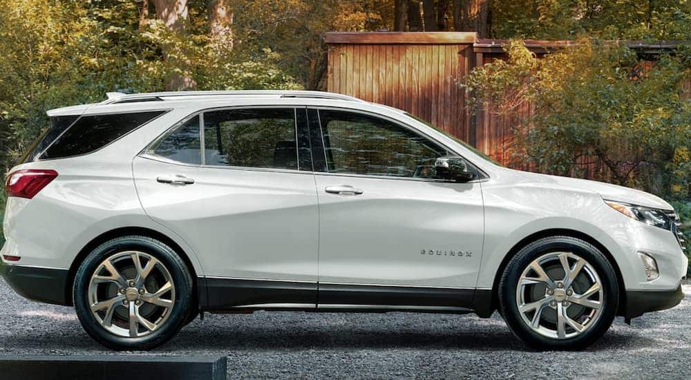 A side view of a white 2020 Chevy Equinox is parked next to a wooden shed.