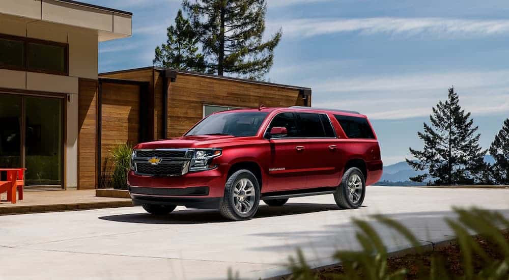 A red 2020 Chevy Suburban, the largest of the Chevy SUVs, is parked at a modern home.