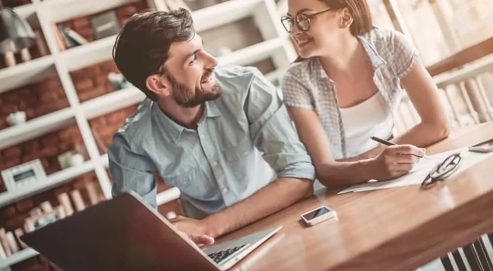 A smiling couple is using their laptop to research extended warranty pros and cons for their car. 