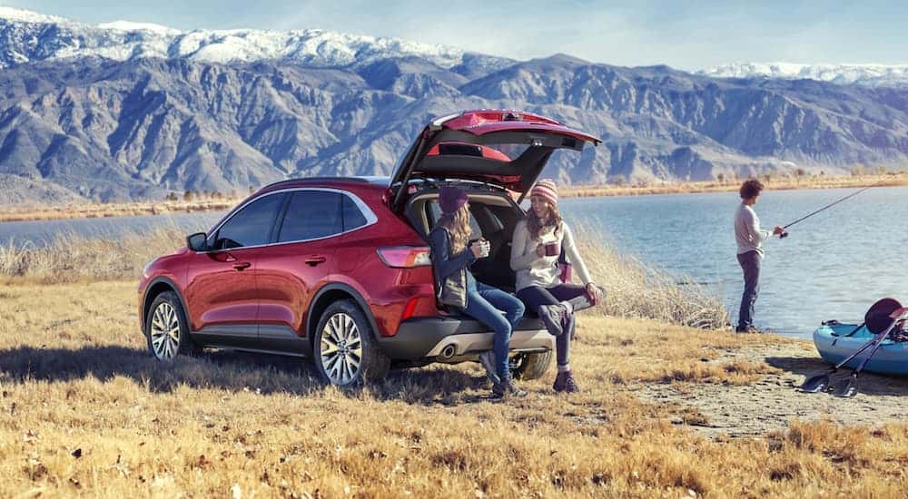 Two gils are sitting in the back of a 2020 Ford Escape while a man fishes at a mountain lake.