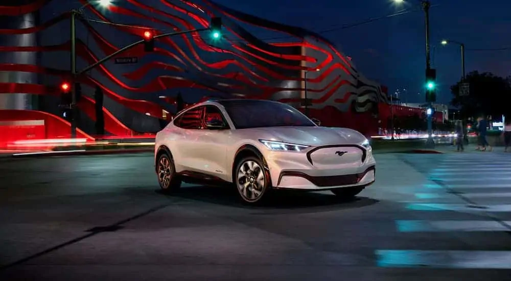 A white 2020 Ford Mustang Mach-E, which is new among Ford SUVs, is parked on a city street at night.