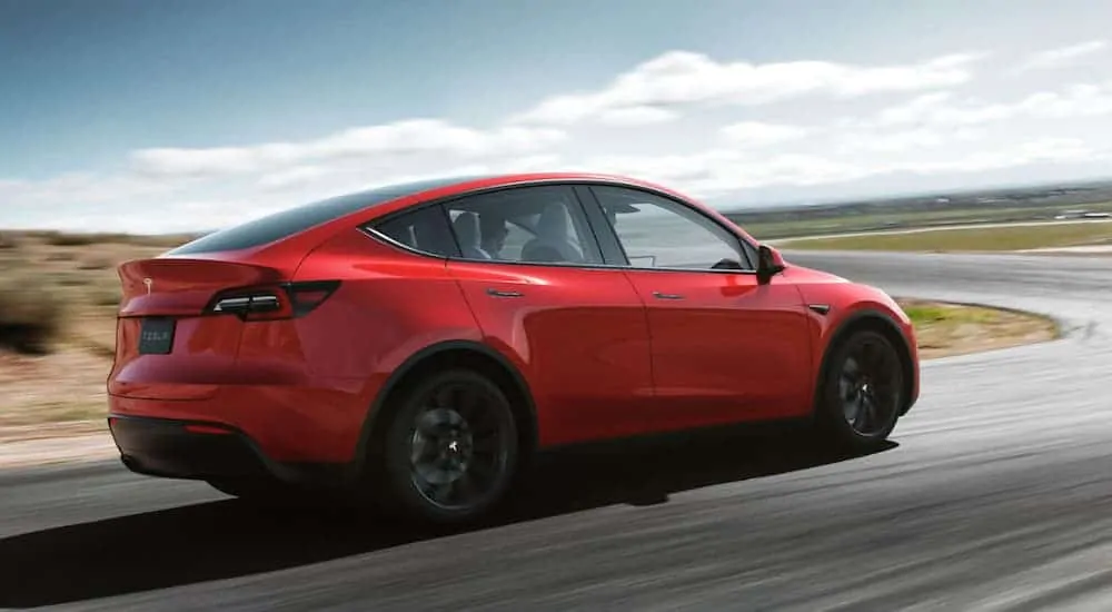 A red Telsa Model Y is driving around a corner on a curvy road.