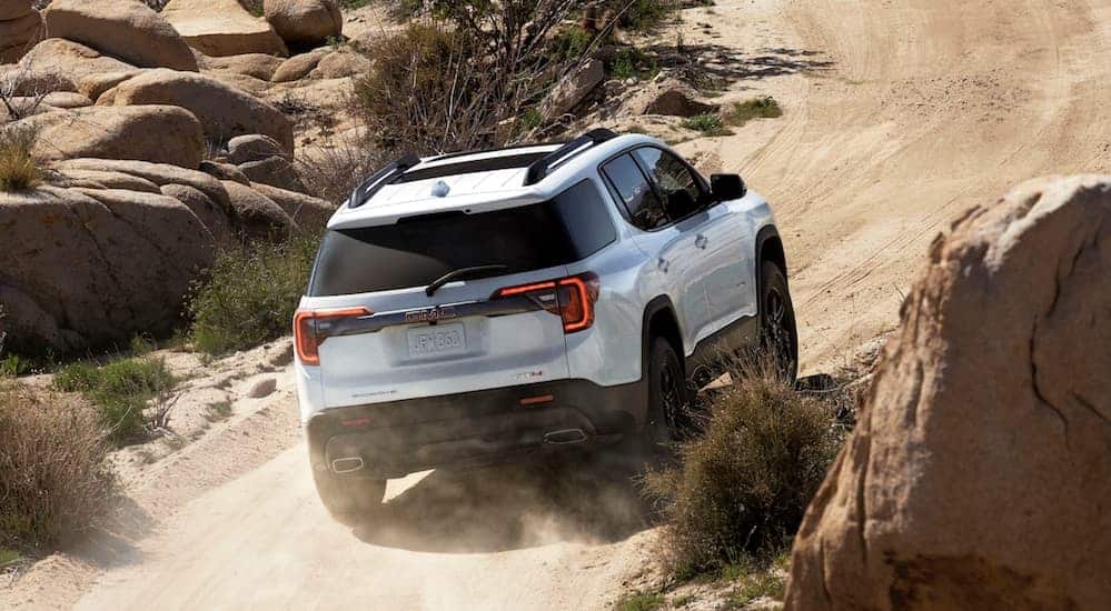 A white 2020 GMC Acadia AT4 is driving up a rock lined dirt hill.