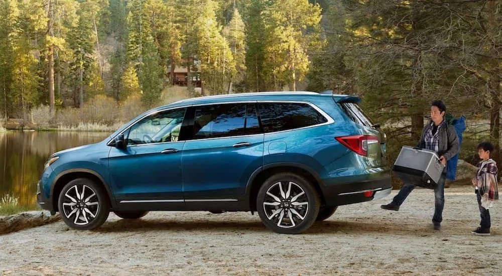 A man and his son are loading up their teal 2020 Honda Pilot at a camp site.