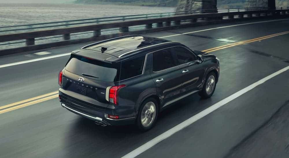 A dark grey 2020 Hyundai Palisade is driving on a highway next to the ocean.