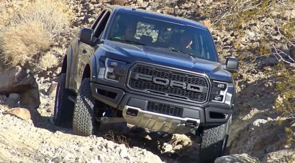 A grey 2017 Ford Raptor, which is a popular model among used Ford trucks for sale, is rock crawling up a rocky hill.