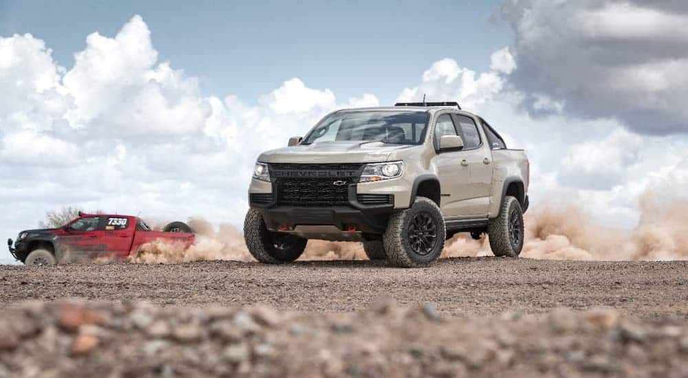 A tan 2021 Chevy Colorado ZR2 is parked in the desert while a red ZR2 Bison races past.