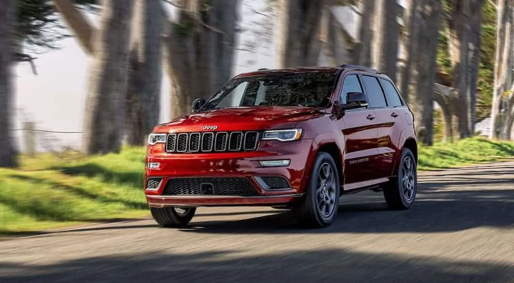 A red 2020 Jeep Grand Cherokee is driving on a tree-lined street.