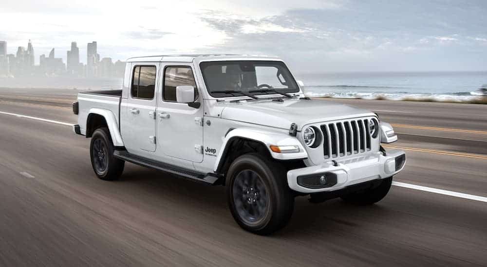 A white 2020 Jeep Gladiator is driving on a highway leaving a city.