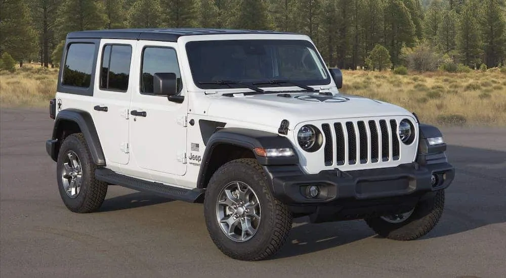 A white 2020 Jeep Wrangler Freedom edition is parked in front of trees.