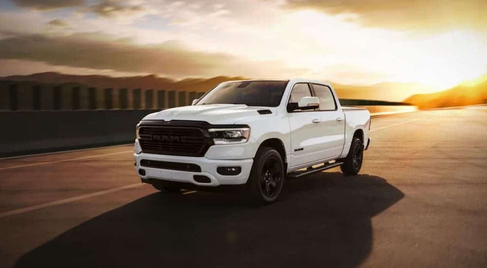 A white 2020 Ram 1500 Night Edition is driving on a highway at sunset.
