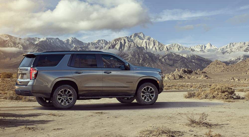 A grey 2021 Chevy Tahoe Z71 is parked on a dirt trail with snow covered mountains in the distance. 