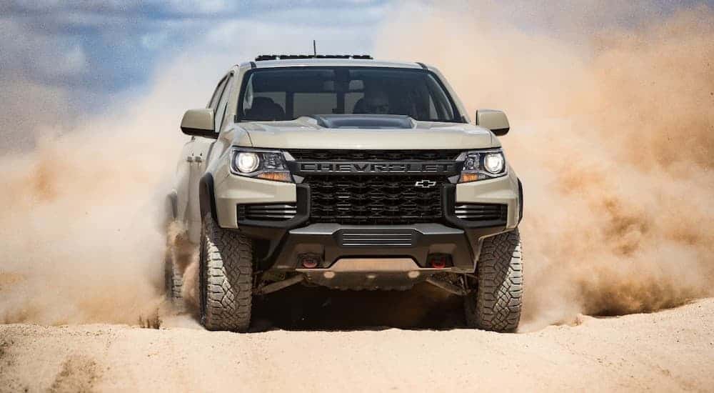 A tan 2021 Chevy Colorado ZR2 is driving on a dirt road and kicking up sand.