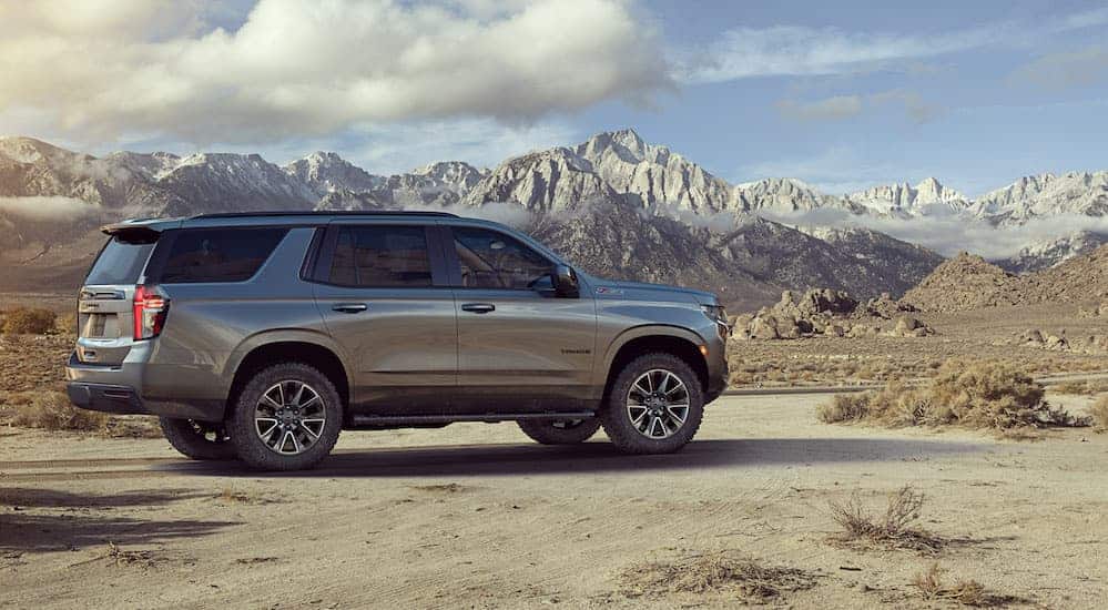 A grey 2021 Chevy Tahoe Z71 is parked on a dirt path with snow covered mountains in the distance. 