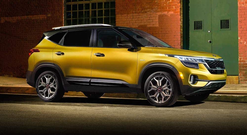 A yellow 2021 Kia Seltos is parked in front of a brick building.