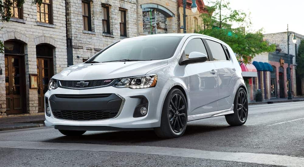 A silver 2020 Chevy Sonic is driving past stone buildings.