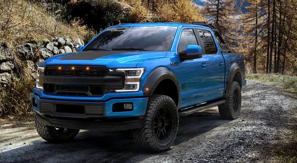 One of the popular Ford Trucks, a blue 2020 Ford F-150 Roush SC is driving on a dirt trail.