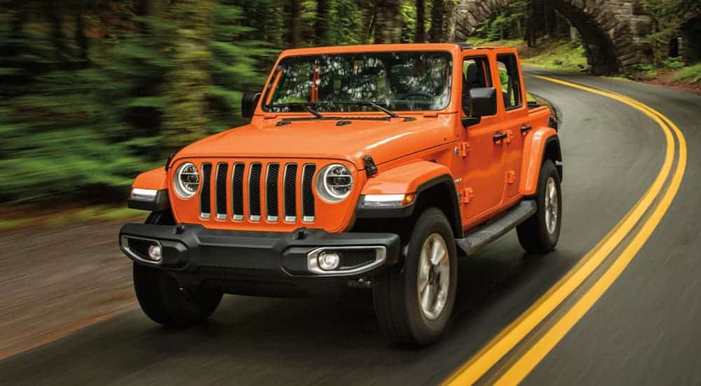 An orange 2020 Jeep Wrangler is driving on a road through the woods.