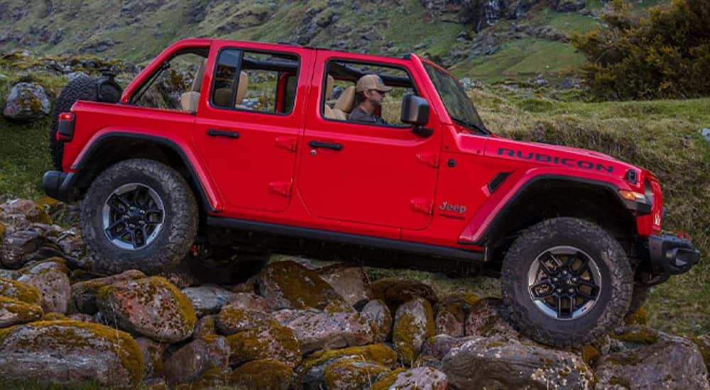A red 2020 Jeep Wrangler Rubicon, which is popular among Jeeps for sale, is off-roading on a rocky trail.