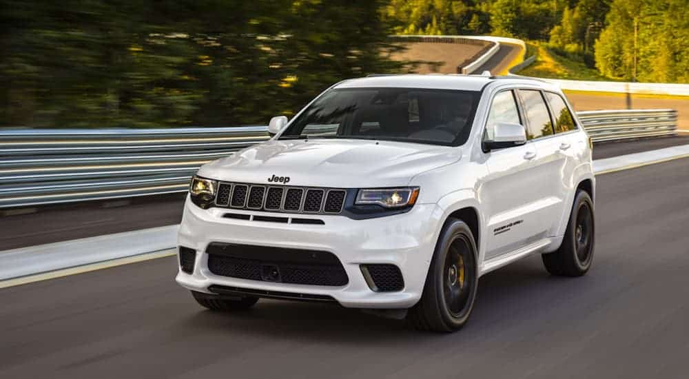 A white 2020 Jeep Grand Cherokee Trackhawk is driving on a tree-lined racetrack.