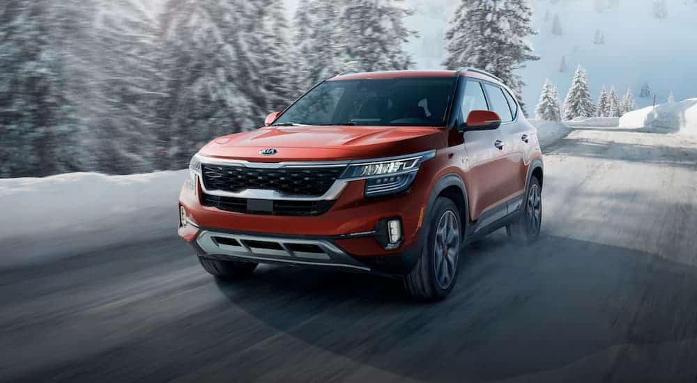 A red 2021 Kia Seltos is driving on a snowy road.