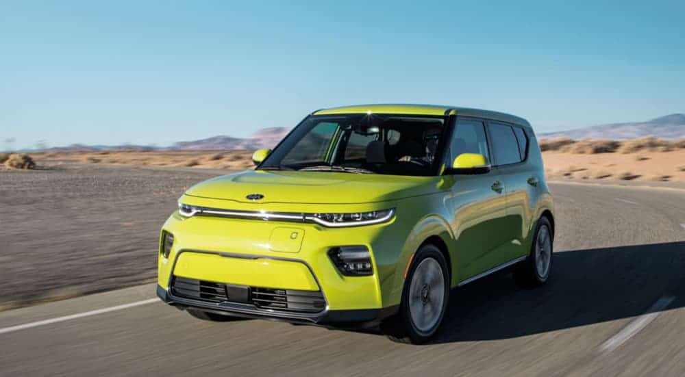 A lime green 2021 Kia Soul EV is driving on a desert road.