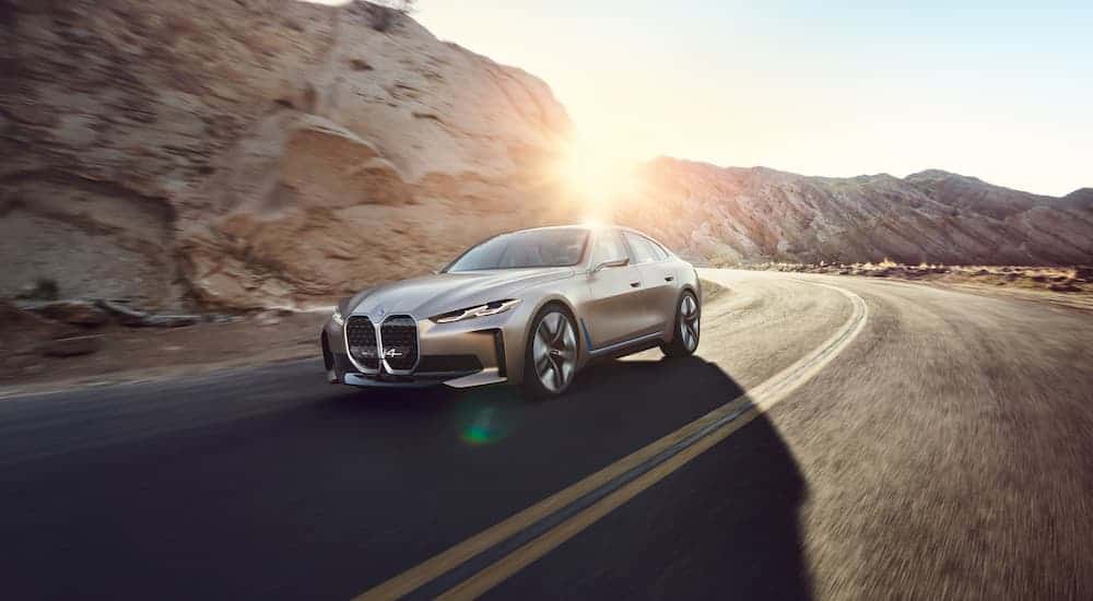 A beige 2021 BMW i4 is driving past a rock face with the sun setting behind it.