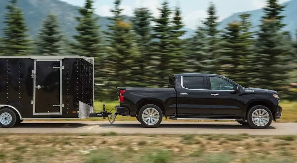 A black 2020 Chevy Silverado is towing a black enclosed trailer past pine trees.